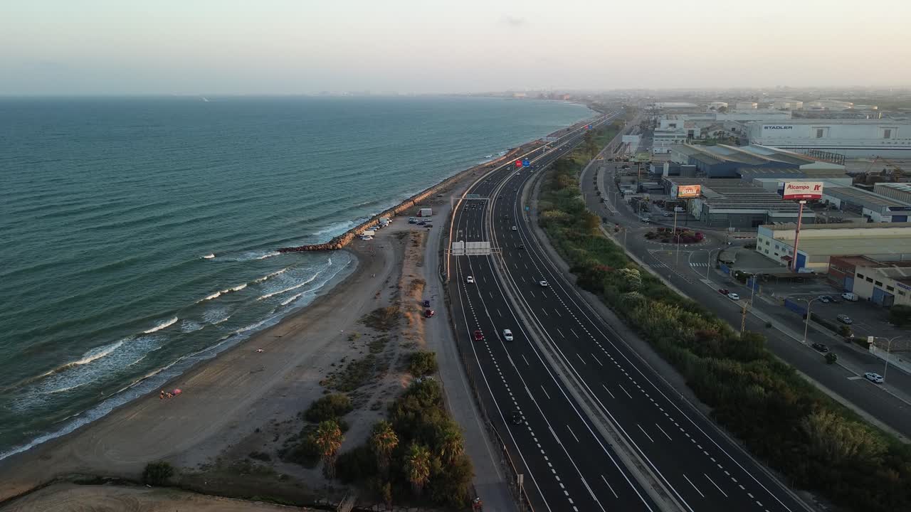 해변에 인접한 여러 차선의 해안 도로의 공중 사진, 반대편에 건물이 있으며, 인프라와 자연 사이의 상호 작용을 보여줍니다.