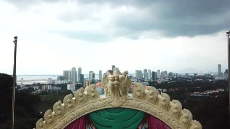 drone shot at a hindu temple, colourful religious art, city scape in the background, malaysia