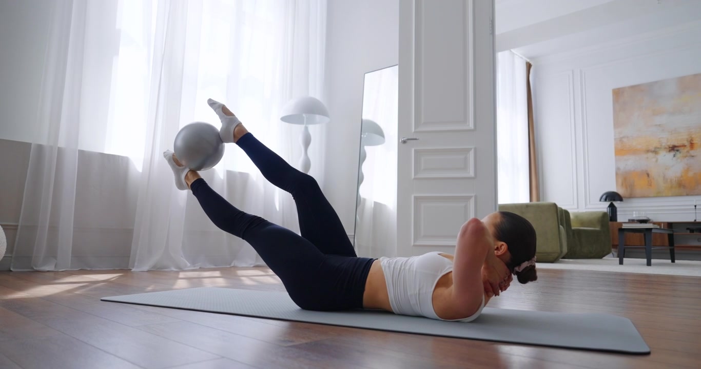 Donna che esegue un esercizio per il core con palla Pilates su tappetino yoga a casa