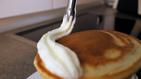 slow motion handheld shot of delicious pancakes being sprayed with a cream dispenser filled with whipped cream for a delicious dessert in the kitchen