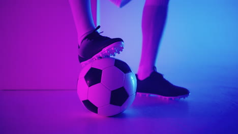 close-up of the foot of a professional black football player standing on the ball in slow motion in the blue-red neon light of the studio. brazilian football player foot on the ball to pose