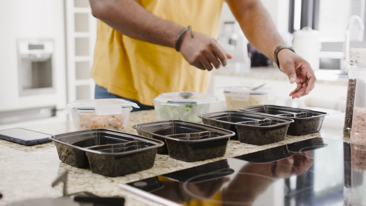 Man placing black trays at counter, scooping food from clear tubs, preparing meals