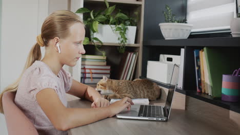 The child is engaged with a laptop in her room, next to her is a red cat