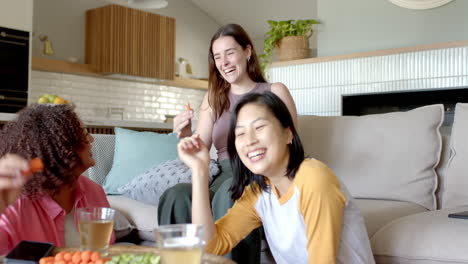 laughing and enjoying snacks, three women friends relaxing together in living room