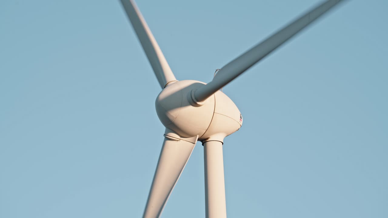 깨한 푸른 하늘을 배경으로 풍력 터빈 허브와 블레이드의 클로즈업으로 청정 에너지를 강조합니다.