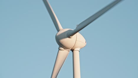 close-up of wind turbine hub and blades against a clear blue sky, highlighting clean energy