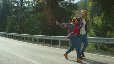 excited friends hiking mountain road. backpackers hold text banner on hitchhike.