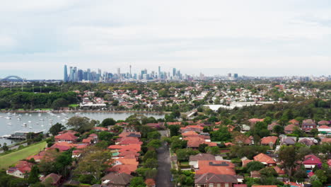 drone aéreo volando hacia atrás sobre casas residenciales con el horizonte de la ciudad en el horizonte en sydney, australia occidental interior