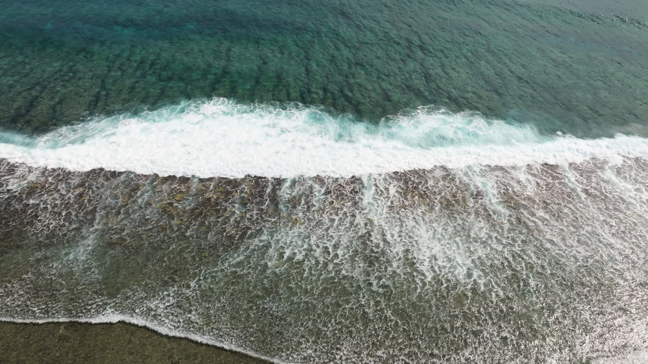 Aerial high angle descends on waves breaking on shallow fringing reef in ocean water