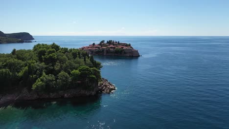 Drone-Volando-Sobre-árboles-Y-Mar,-Centrándose-En-La-Península-De-Sveti-Stefan