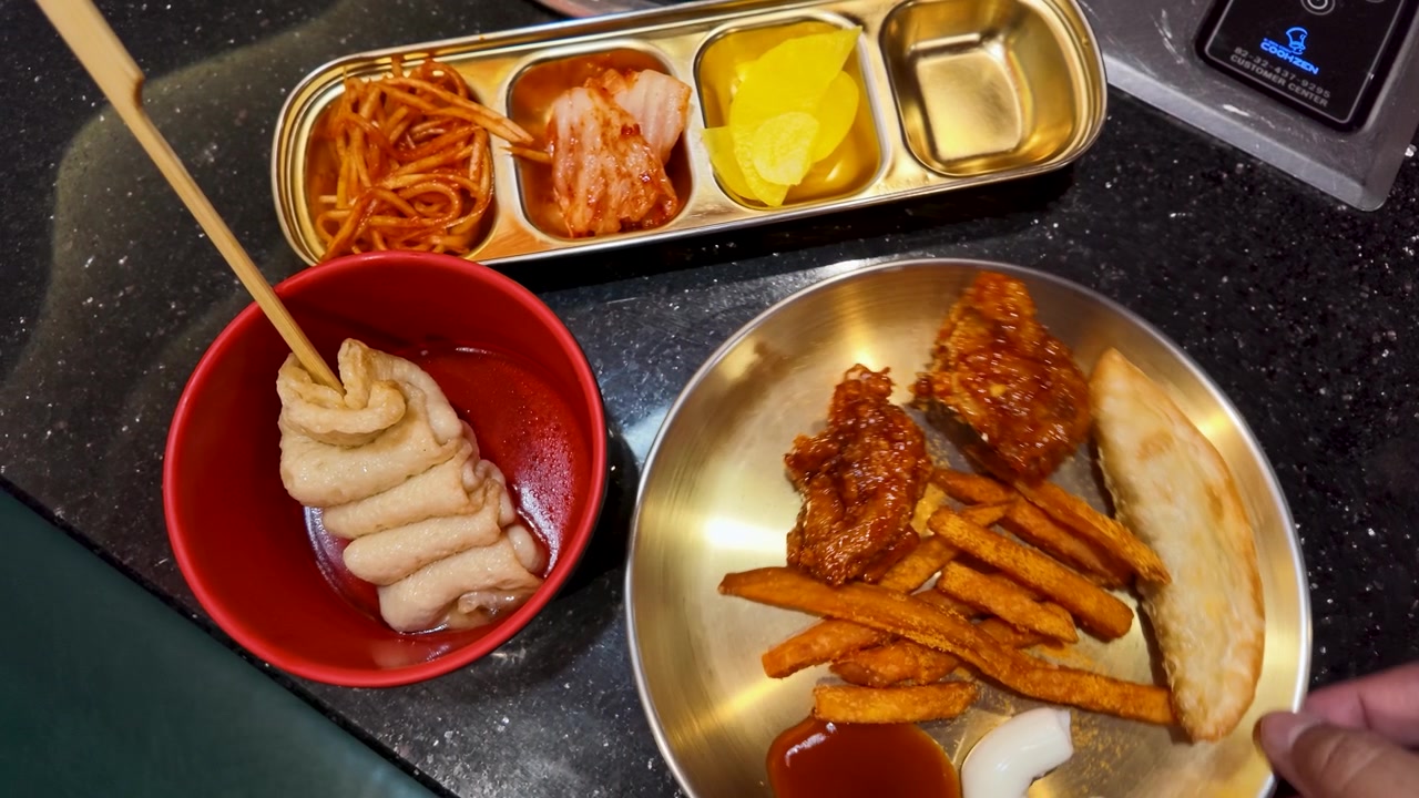 Tampak atas masakan Korea termasuk kimchi, ayam goreng, dan sate kue ikan di atas piring