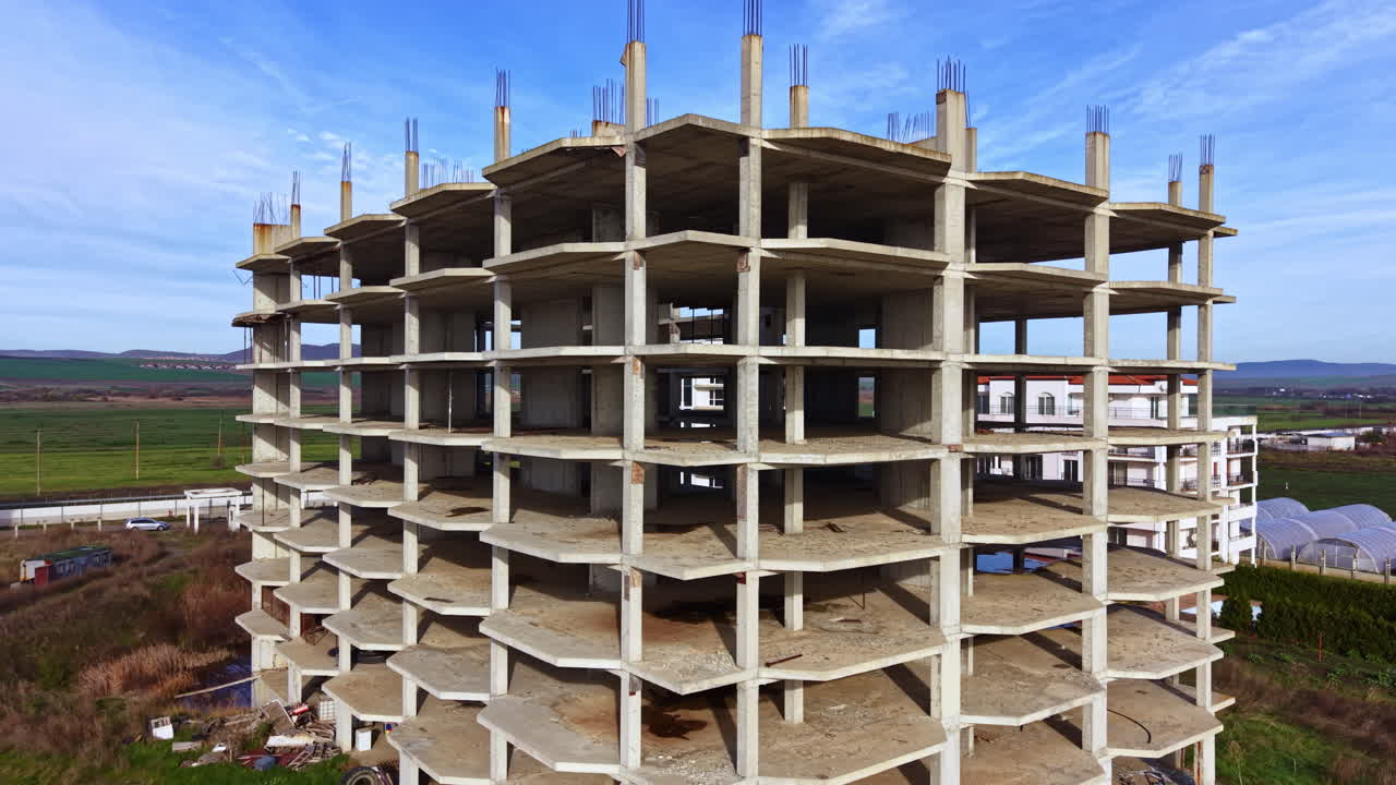 Construction site showcasing a half-finished concrete building under a clear blue sky in a rural landscape near the coast, illustrating the essence of urban development and nature's backdrop