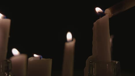 an extreme close up and pan across of white candles lit with a black background