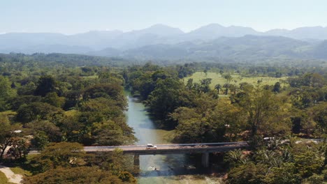 vehículo terrestre blanco con tienda en el techo cruzando un puente sobre un río poco profundo cortando a través de bosques y bancos bordeados de árboles