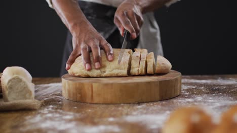 video of cook cuts the loaf of bread on black background
