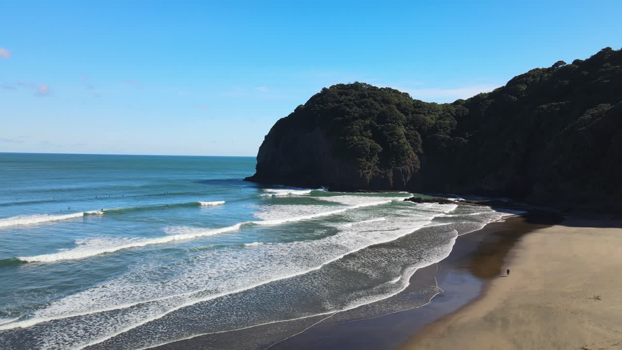 panorámica aérea cinematográfica con surfistas esperando el próximo conjunto de olas en la playa de arena negra