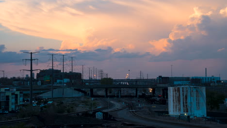 Vívido-Timelapse-De-La-Puesta-Del-Sol-Del-Tren-De-Carga-Y-El-Tráfico-Sobre-El-Puente-Del-Ferrocarril,-Denver