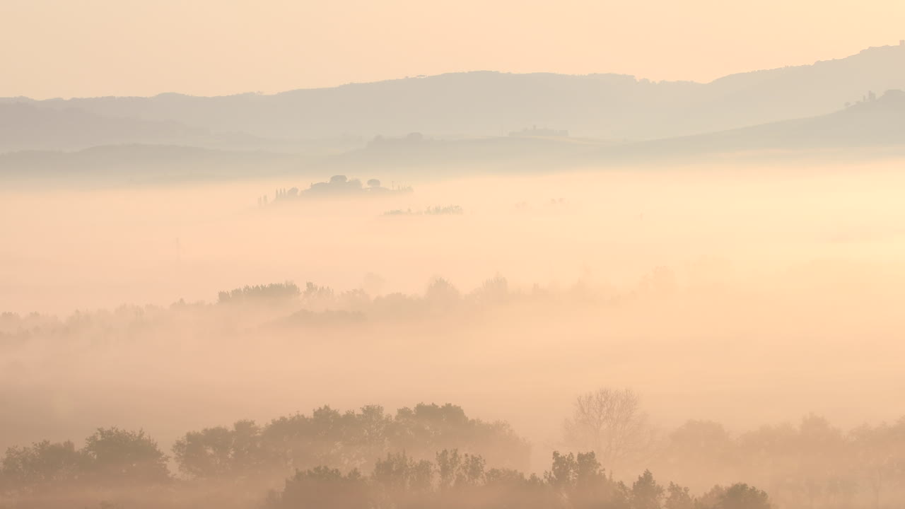 A misty dawn over the rolling landscape of the Val d'Orcia in Tuscany, Italy