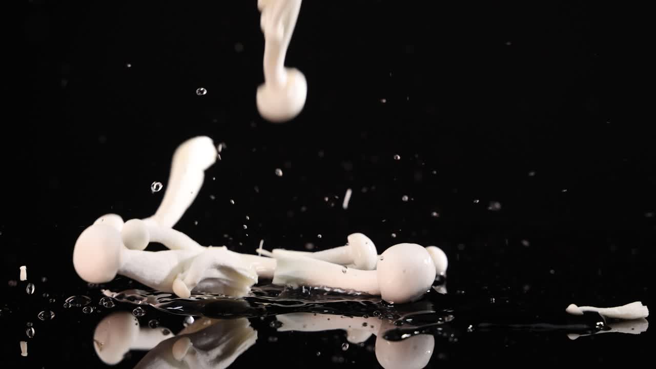 White mushrooms fall and scatter onto a glossy black surface, captured in high-speed slow motion with dramatic lighting and a clean, minimal background