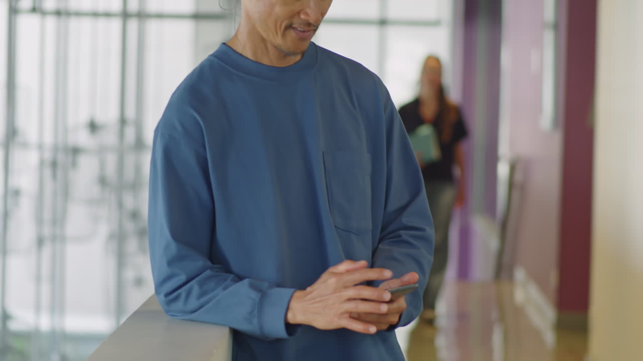 Asian Man Messaging on Phone in Office Center