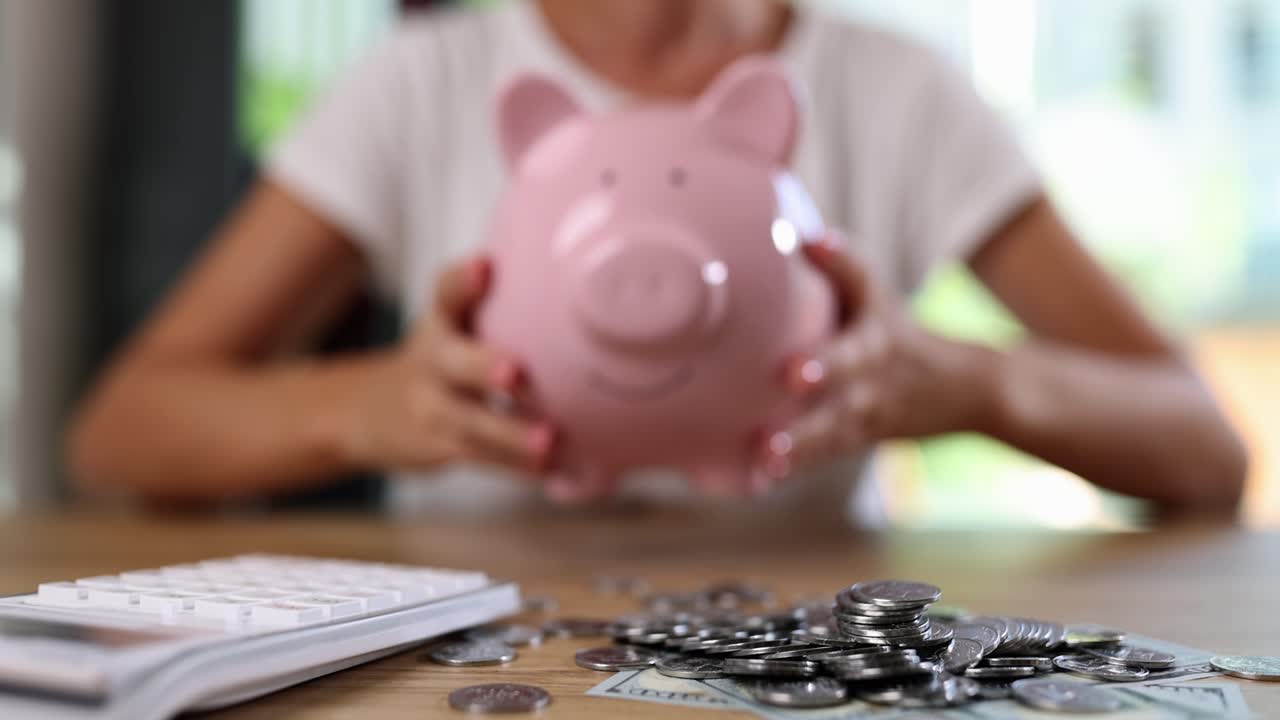 Person holding a piggy bank with coins and calculator on a table