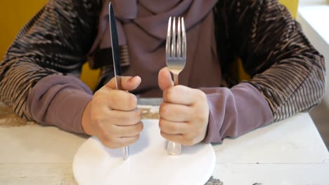 women hand holding cutlery with empty plate on wooden table at acfe
