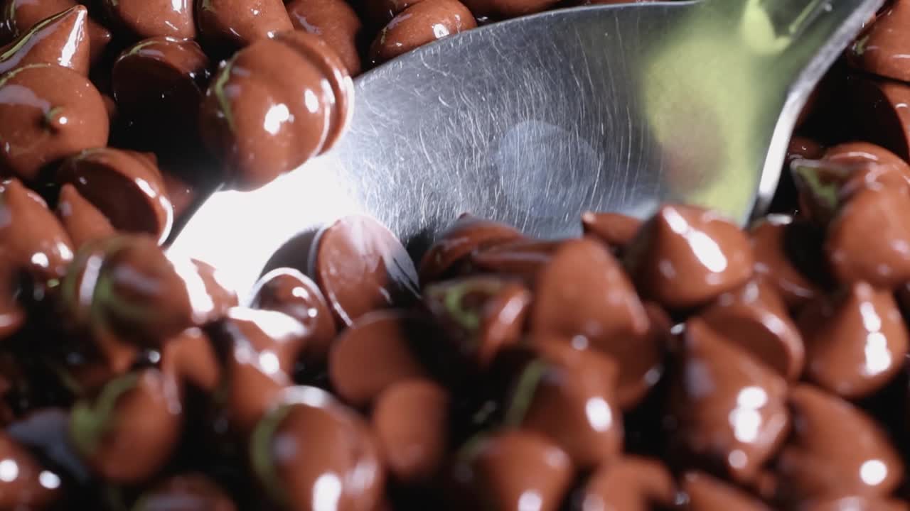 A detailed view of glossy chocolate chips being scooped with a metal spoon.