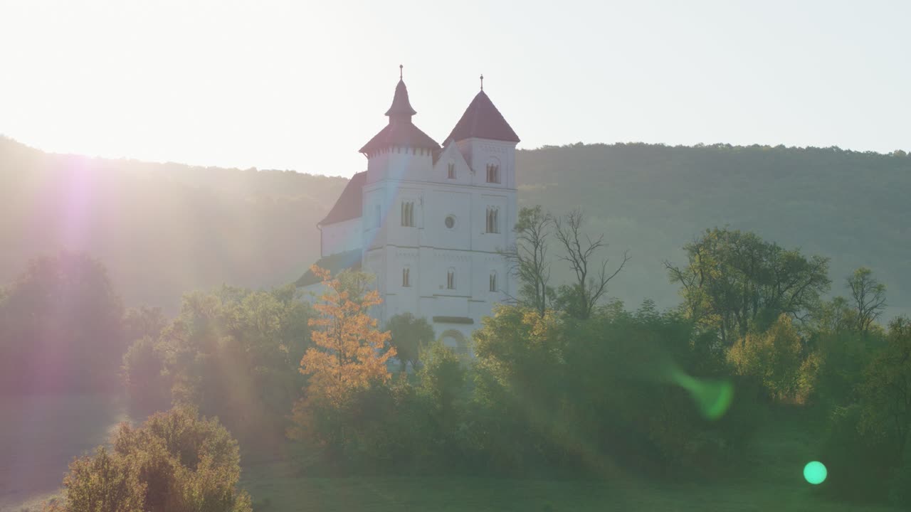 Aerial photo of a white church with red roofs on a hill, in a foggy morning landscape. Herina, Bistrita Nasaud, Romania