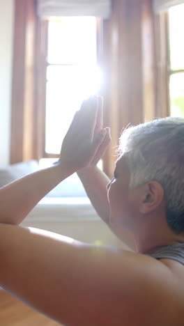 vertical video of focused senior biracial woman meditating at home, slow motion