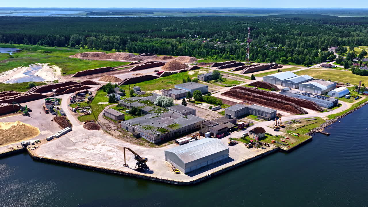 Mērsrags Port, Latvia showing timber storage, warehouses, and forested coastline by the Baltic Sea - Aerial parallax view