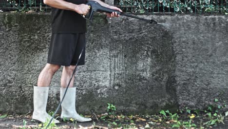 man using electric powered pressure washer to power wash dirty concrete wall