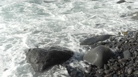 close-up of wave rolling in on black rocky stone beach