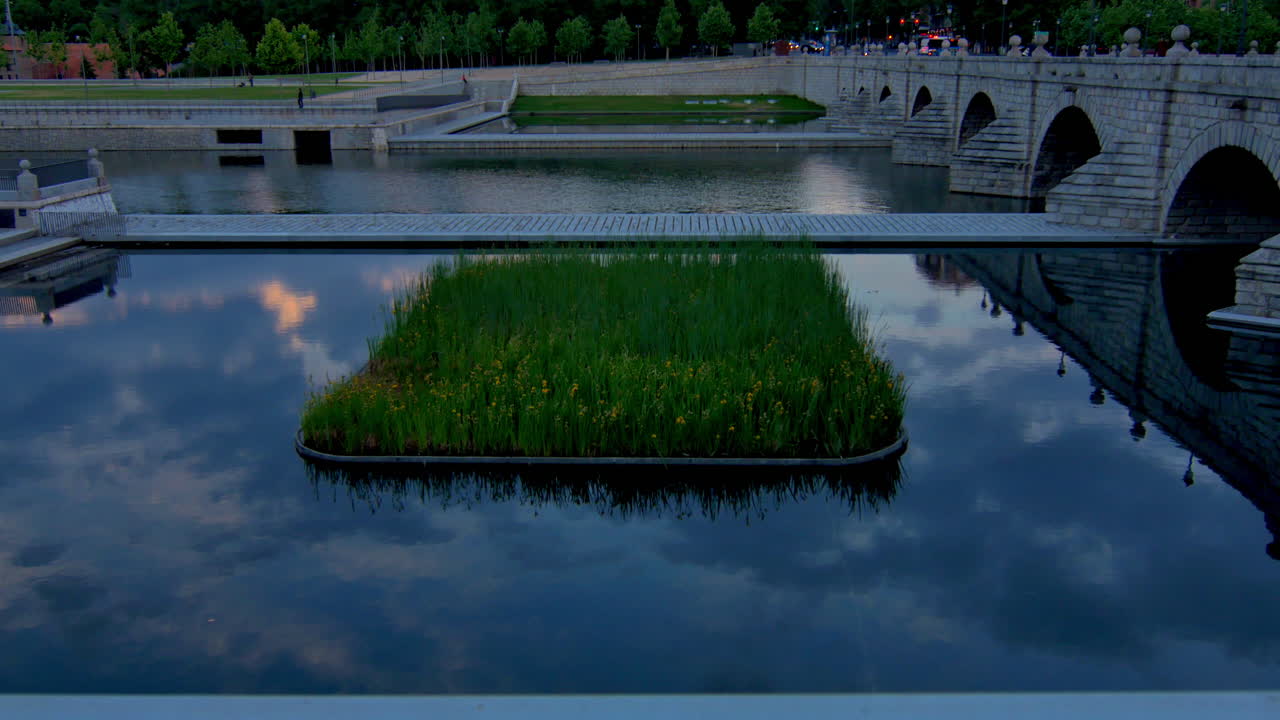 Golden light reflects in still water among green islands and stone bridges, capturing a poetic moment at dusk in the city.
