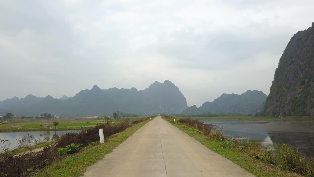 Cinematic narrow road, reflecting lake and rice fields with grass and big mountains in background
