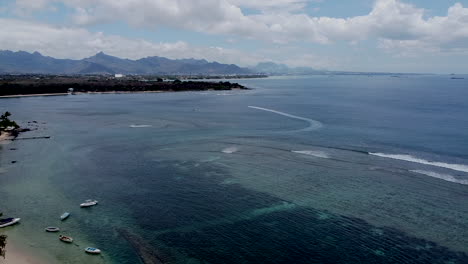 Aerial-backwards-flight-of-epic-tropical-coastline-beside-clear-indian-ocean-with-many-boats