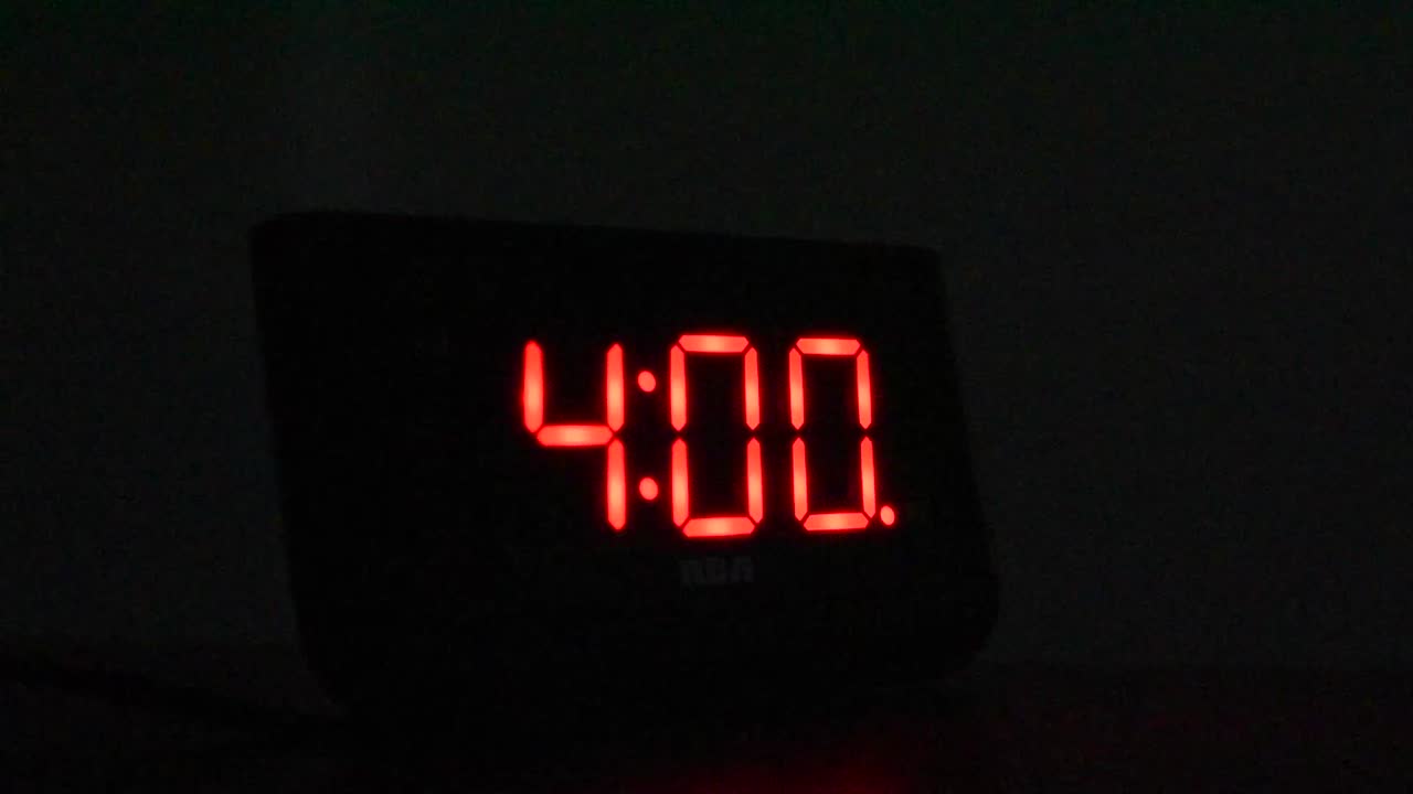 Alarm clock going off at 4:00 AM in dark room. Hand reaches out and stops alarm