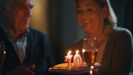 a senior man is blowing a candles of a cake made with love by his wife for a birthday celebration at home.