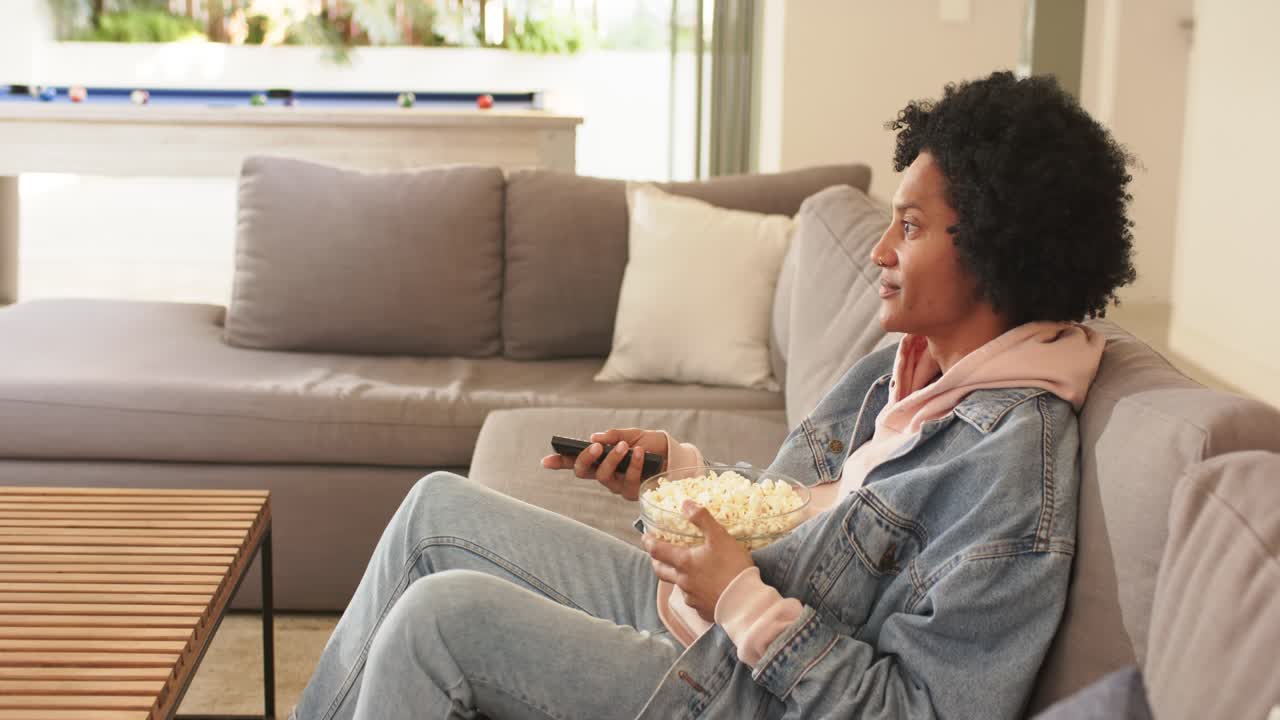 Mand, der tager popcorn fra en skål og zapper rundt på fjernsynet med fjernbetjeningen i stuen. Plads til tekst