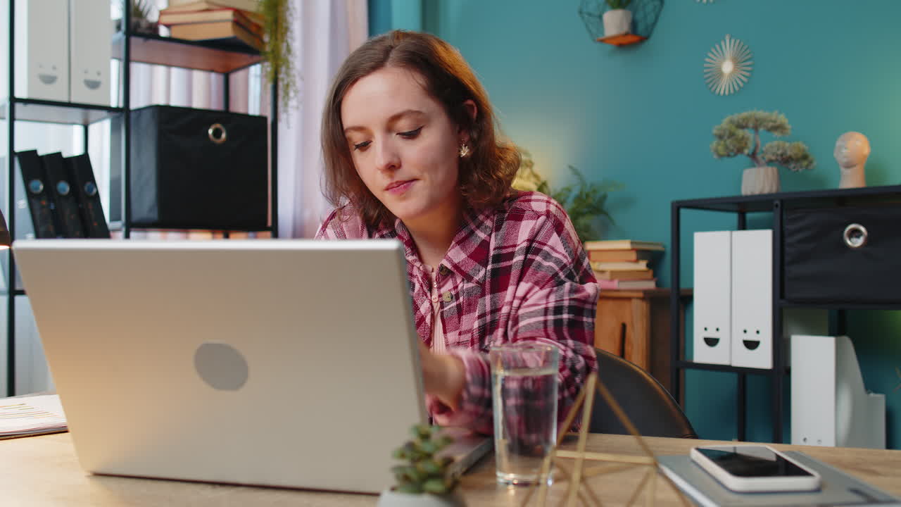Businesswoman girl sitting at workplace desk drinking water while working with laptop in home office