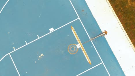 rising from basketball hoop on a blue court at an empty park