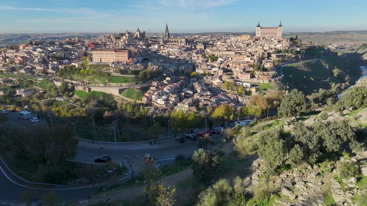 Ilmakuva droonilla kuvattuna Toledon yläpuolelta, Espanjasta. Kuvassa näkyy Tagus-joki pienen vesiputouksen kera ja kaupungin siluetti taustalla kirkkaan marraskuun taivaan alla.