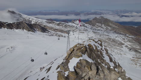vuelo aéreo a lo largo de la bandera austriaca en el pico de la montaña y ascensor en el valle nevado de los alpes