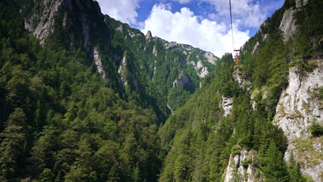 Cable car through mountain valleys. Visitors enjoy a cable car journey across steep cliffs and dense green forests under a bright blue sky
