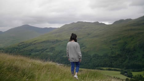 Young-woman-walking-in-Scottish-highlands-raises-arms,-turns-and-smiles