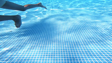 bottom of the swimming pool. clear water background with the reflection of sun rays underwater. someone swims in the pool. amazing view from underwater camera.