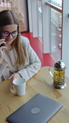 lady wearing light suit having tea in office. businesswoman speaking on the phone during her lunch break. high angle view. vertical video