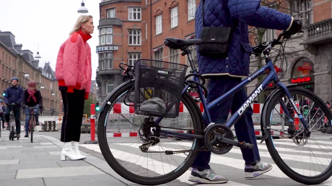 Caucasian woman walks bicycle across street in downtown Copenhagen city crosswalk, Denmark, low angle slow motion