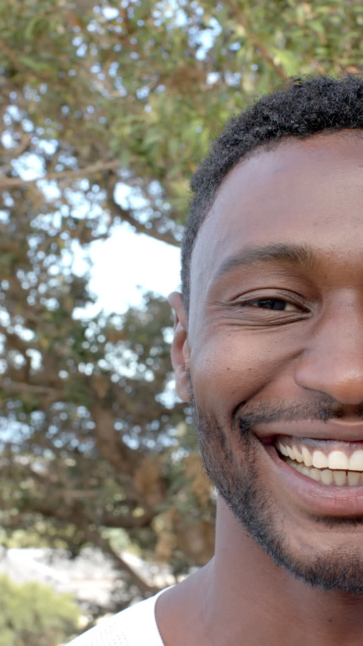 Vertical video: Smiling man outdoors with trees in background, enjoying nature and fresh air