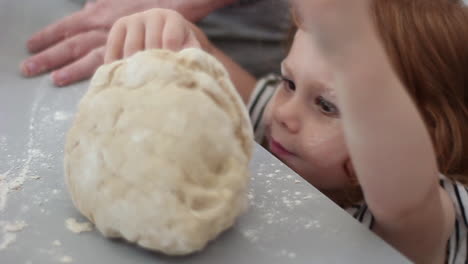 pre-school girl with a handful of dough and a face full of flour helping mom make a make in the kitchen