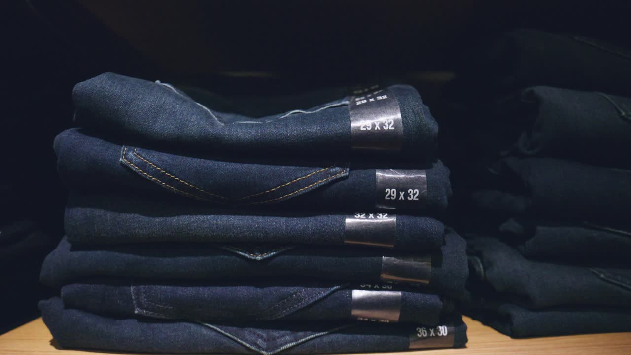 Pile di jeans di diverse taglie, stili e colori su scaffali per l'esposizione e la vendita